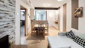 A modern living room with a sofa, a dining table with chairs, and a kitchen in the background.