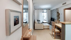 A modern living room with a sofa, a dining table with chairs, a TV, and a stone wall.