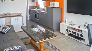 Une cuisine moderne avec des meubles gris, un micro-ondes blanc et un grand téléviseur à écran plat fixé au mur.