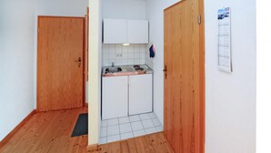 Cucina compatta con mobili bianchi, lavello e piano cottura. Sono presenti porte in legno su entrambi i lati e un piccolo tappetino sul pavimento.