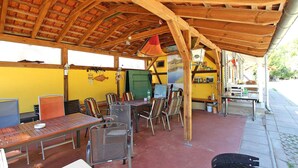 An outdoor patio with wooden beams, metal chairs, a table, and a grill. - Ferienhaus Rheinsberg (Rheinsberg OT Zechline)