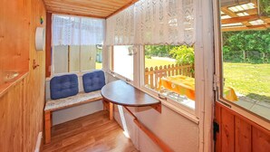 A cozy cabin interior with a wooden bench, a small table, and a view of a garden through a window. - Ferienhaus Rheinsberg (Rheinsberg OT Zechline)