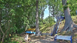A park with a wooden bench, a blue staircase, and a yellow kayak. - Ferienhaus Rheinsberg (Rheinsberg OT Zechline)