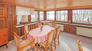 Un comedor acogedor con una mesa redonda, sillas de madera y vistas a árboles a través de amplios ventanales.