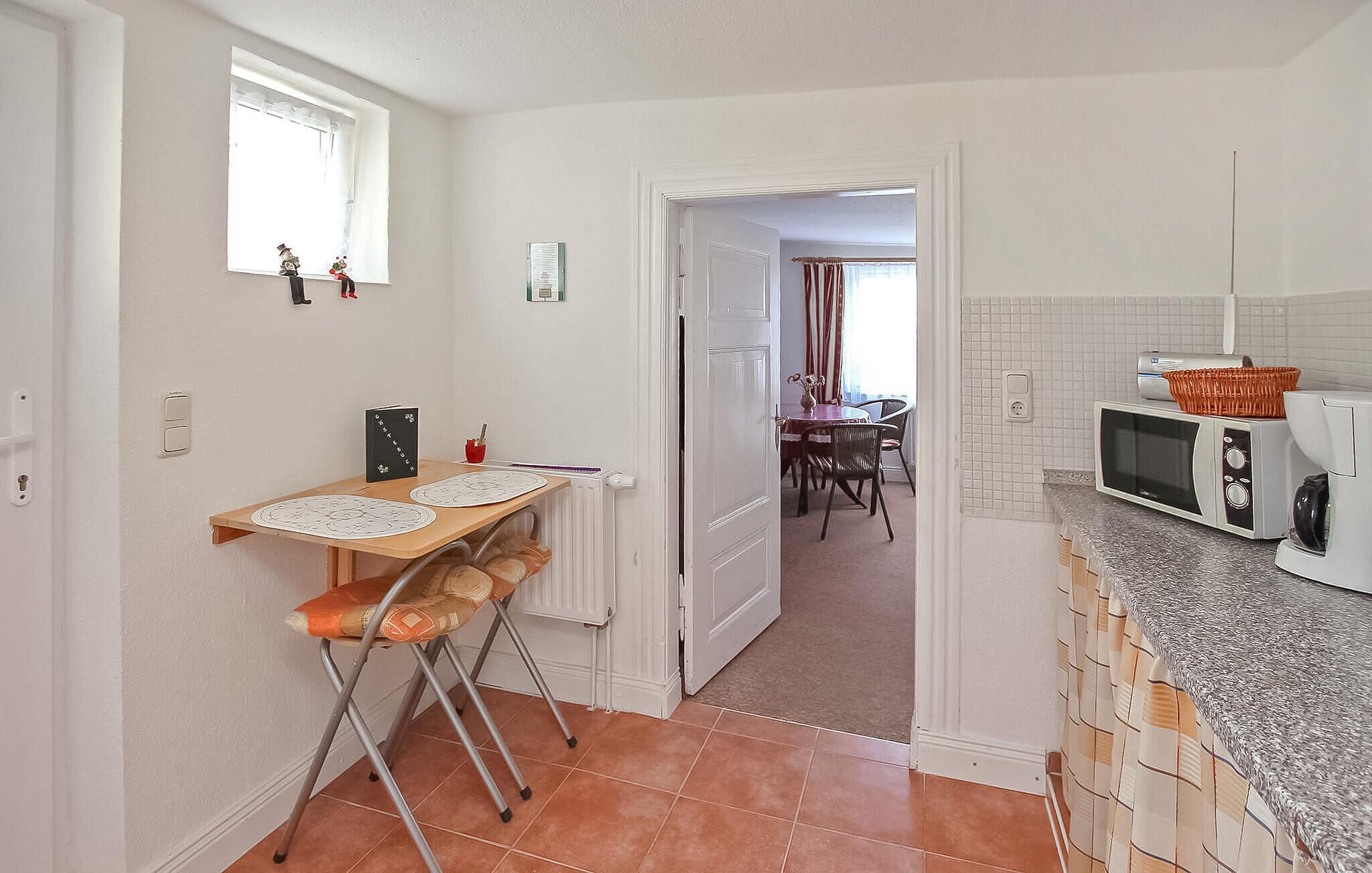 A narrow kitchen with a dining area in the background.