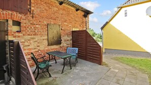 Een terras met een bakstenen muur, een geel gebouw en een houten poort.