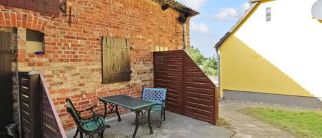 A patio with a brick wall, a yellow building, and a wooden gate.