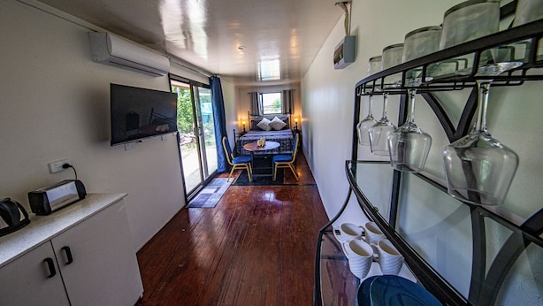 Un pasillo estrecho con una cama, un televisor y un mueble para cristalería.