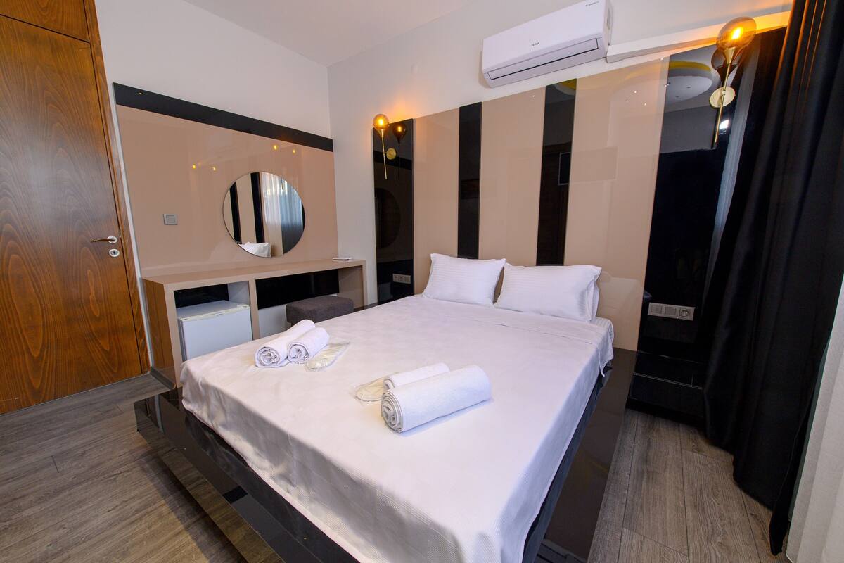 Una habitación de hotel con cama, escritorio, espejo y unidad de aire acondicionado.