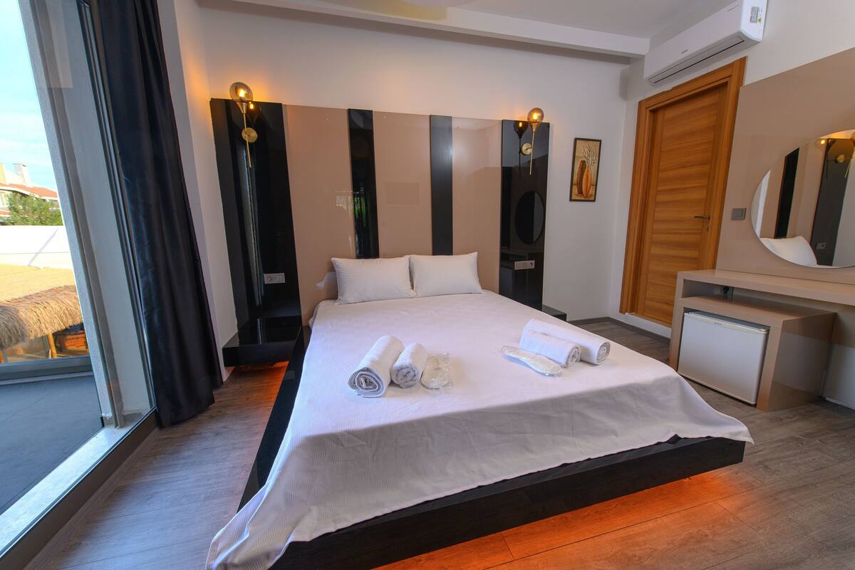 Una habitación de hotel moderna con una cama grande, un escritorio pequeño, un espejo y una puerta corredera al exterior.