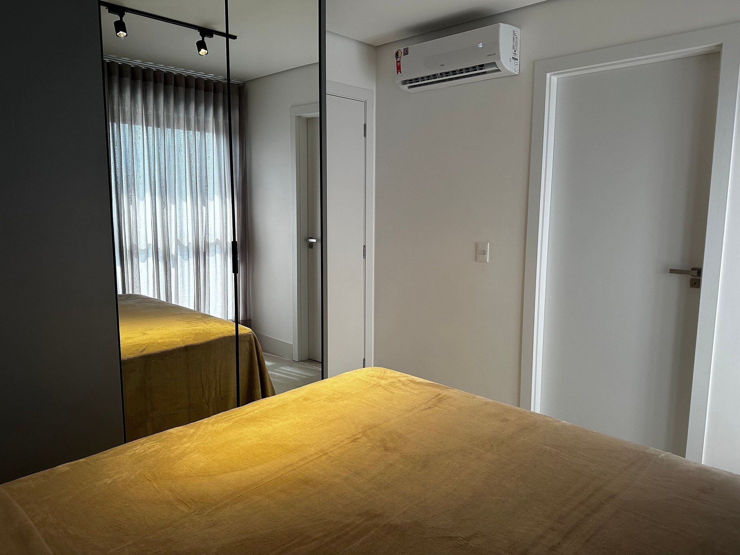 A room with a bed, a window with curtains, an air conditioning unit, and a door.