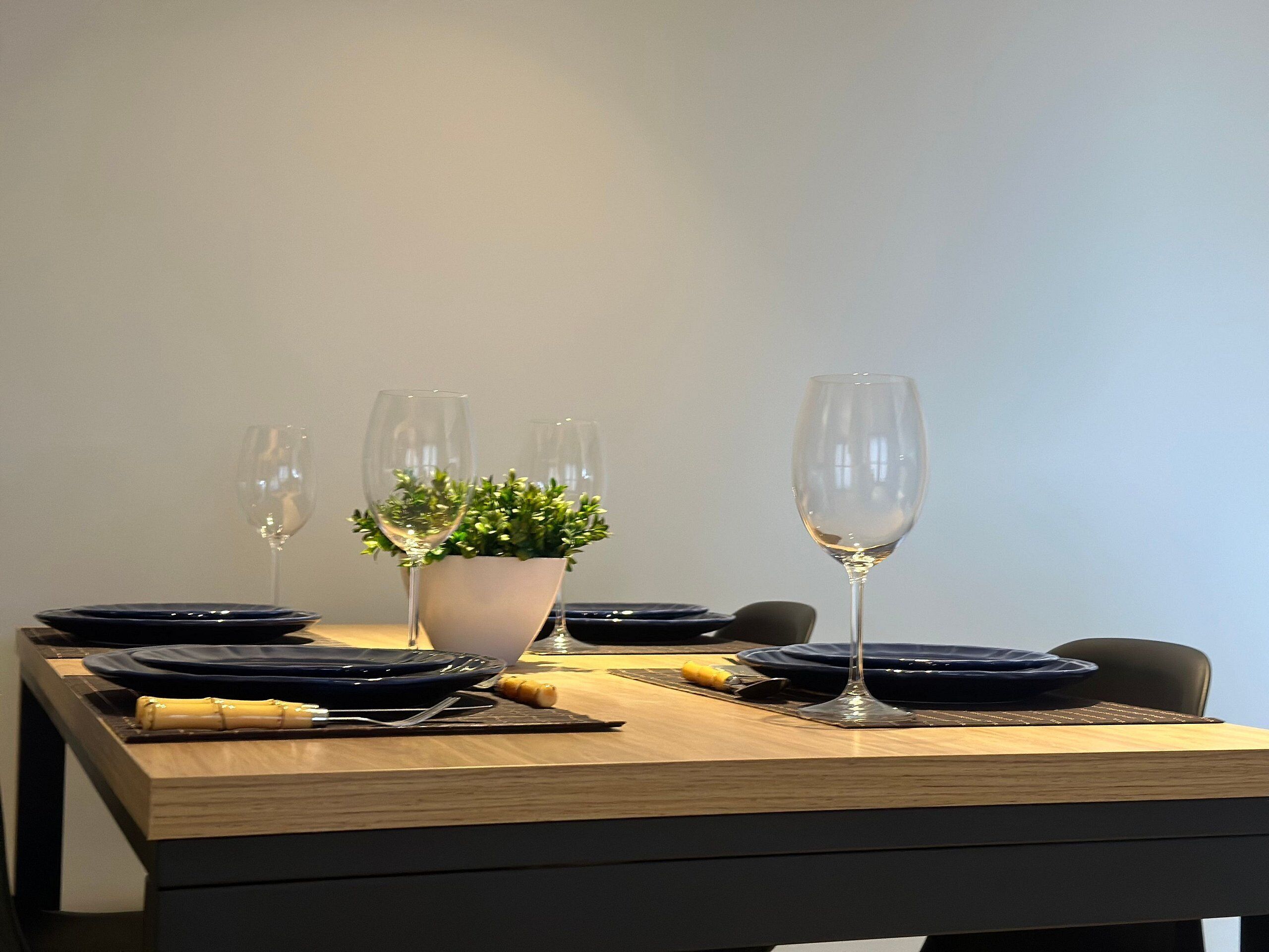 A dining table set with plates, cutlery, and glasses, with a potted plant in the center.