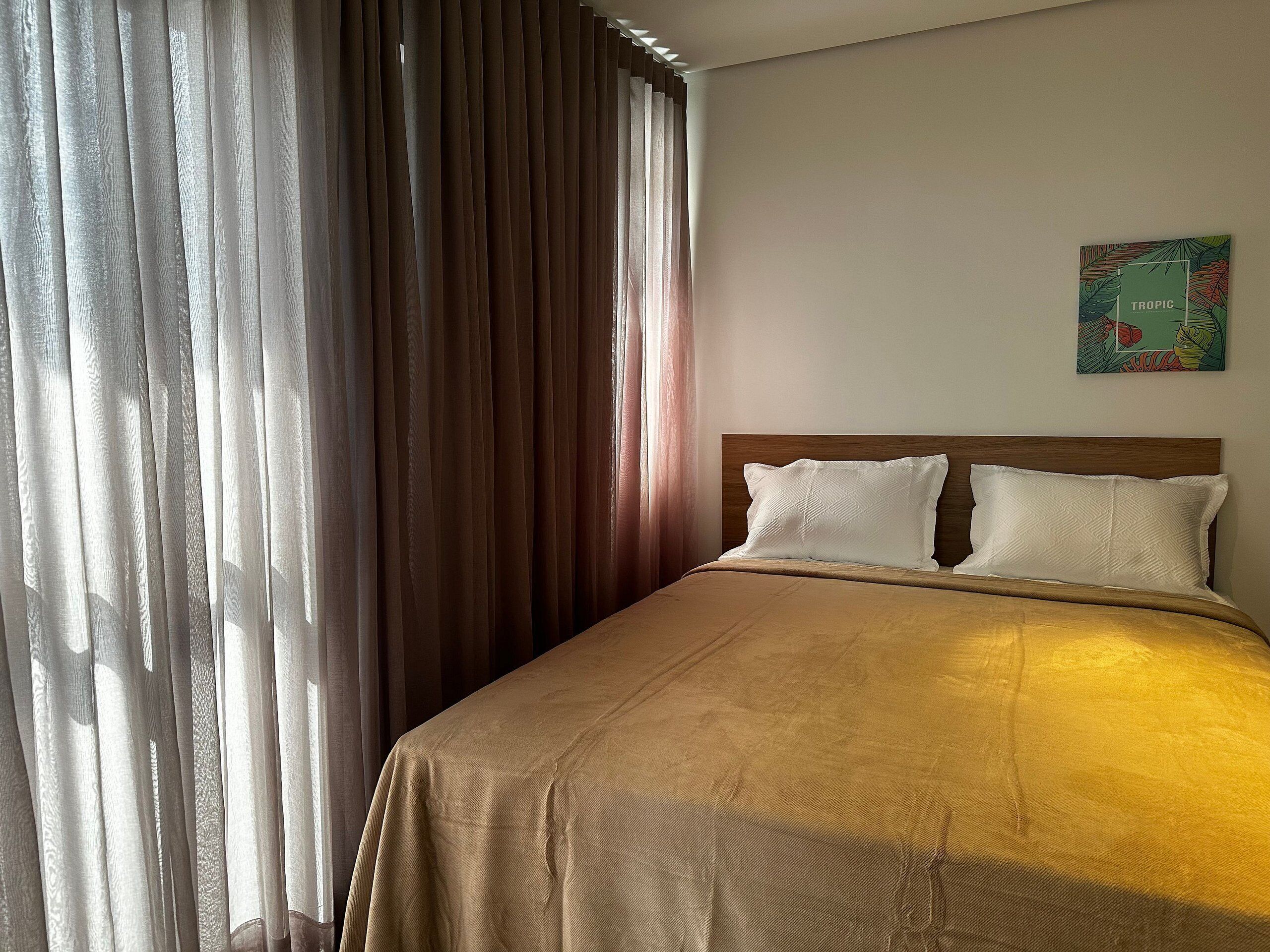 A hotel room with a bed, curtains, and a wall art piece.