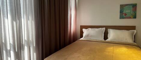 A hotel room with a bed, curtains, and a wall art piece.