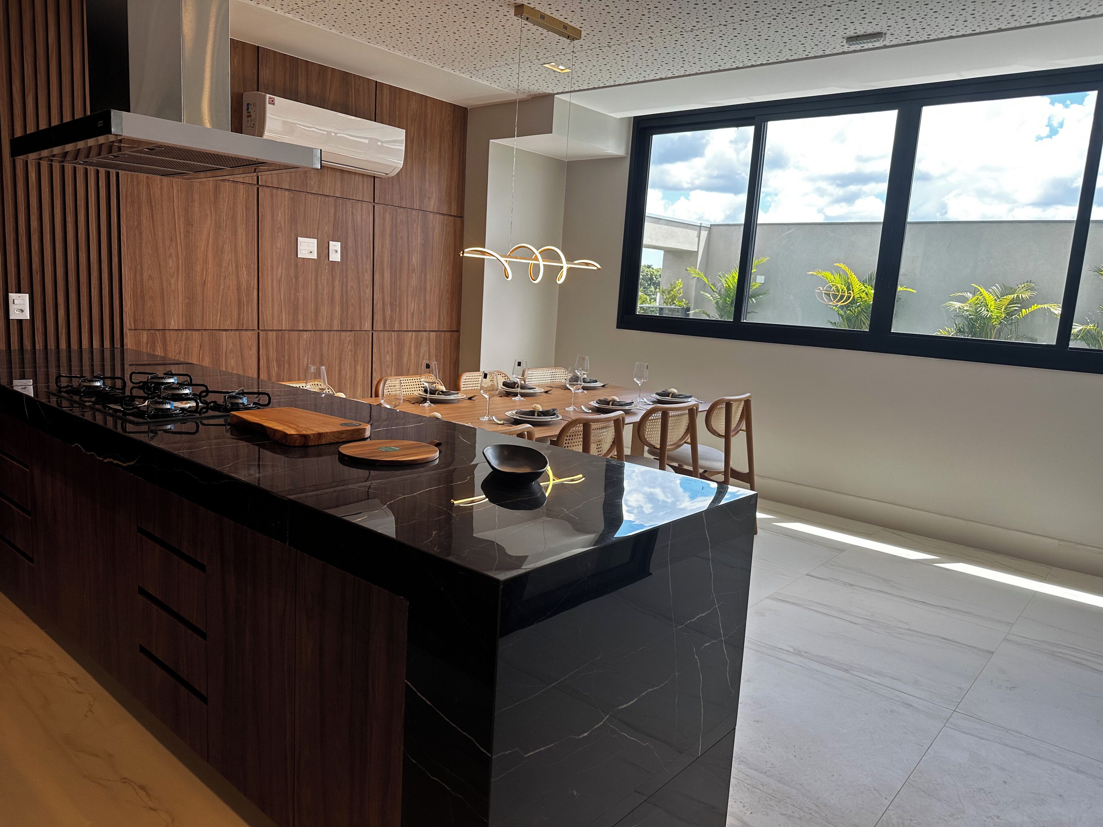 Une cuisine moderne avec un îlot central en marbre noir, des armoires en bois et une grande fenêtre donnant sur un espace verdoyant.
