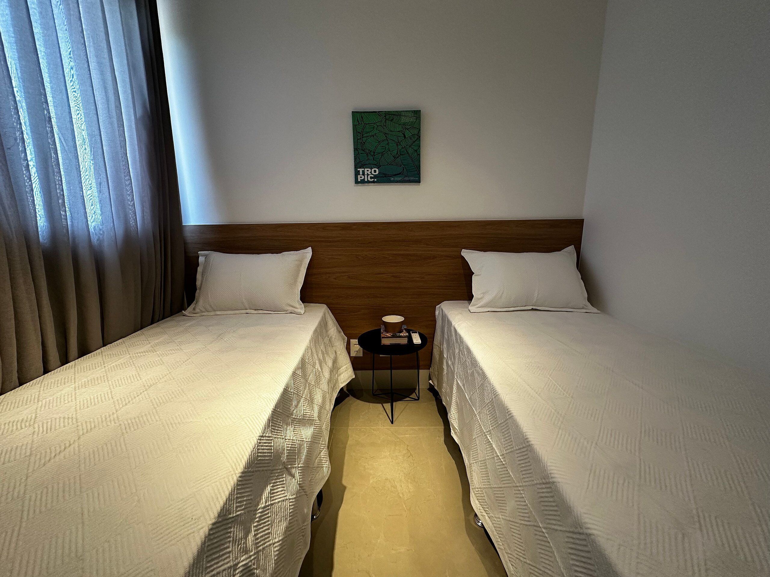 Habitación de hotel con dos camas, una mesita con una lámpara y una obra de arte en la pared.