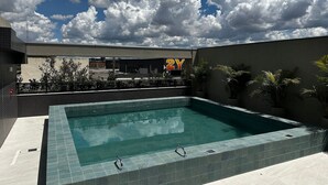 A swimming pool with a tiled edge, surrounded by a low wall and potted plants. - PARK SUL - Edifício Essence (Guará)