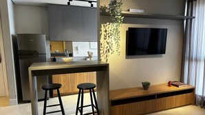 A modern kitchen with a built-in refrigerator, a bar counter with stools, a sink, and a potted plant. - PARK SUL - Edifício Essence (Guará)