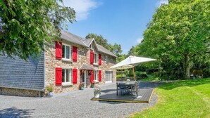 Una casa de piedra con contraventanas rojas, un patio con mobiliario exterior y un jardín.
