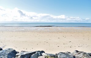 Une plage avec un rivage rocheux et une mer calme sous un ciel partiellement nuageux.