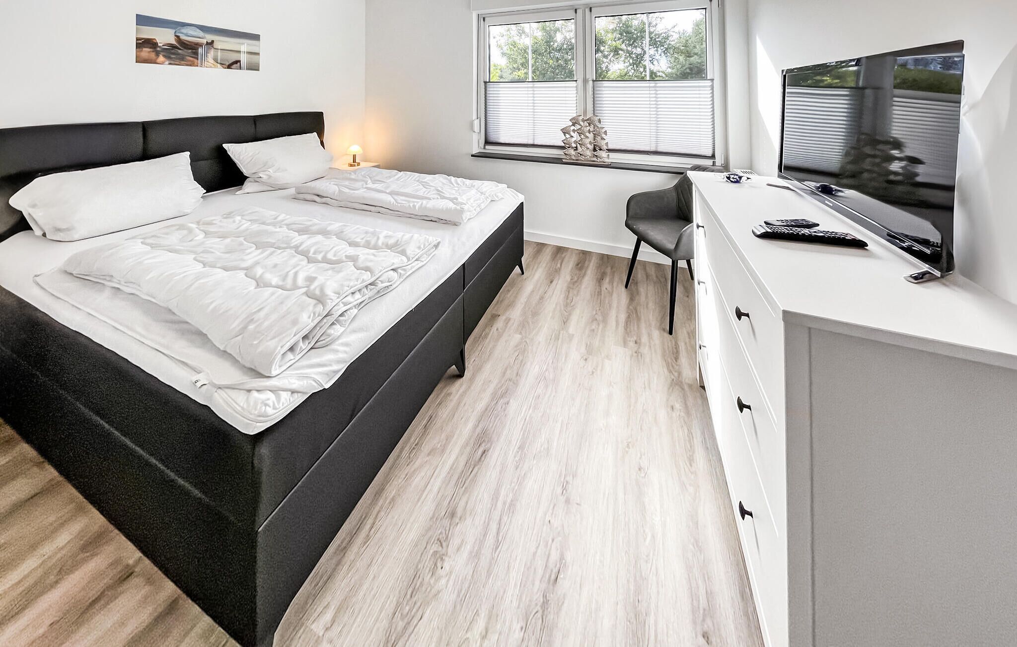 A bedroom with a bed, bedside table, desk, chair, and a TV.