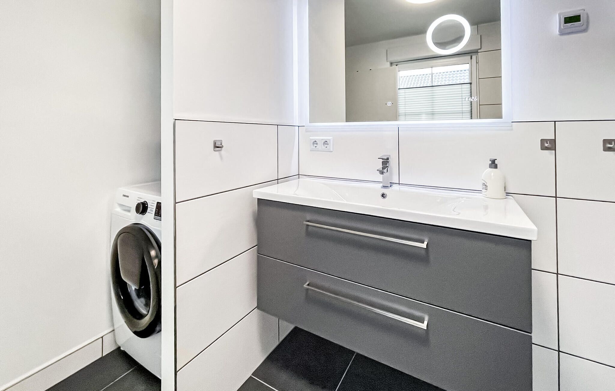 Une salle de bain moderne équipée d’un lave-linge, d’un lavabo avec un miroir et de toilettes.