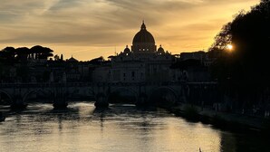 Vista del atardecer de un edificio histórico con una cúpula, un puente y un río.