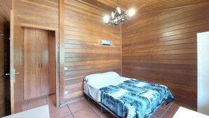 A bedroom with wooden paneling, a bed with a patterned bedspread, a ceiling light fixture, and a door.