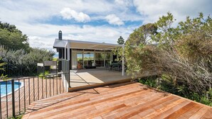 A modern house with a wooden deck, a pool, and a garden.