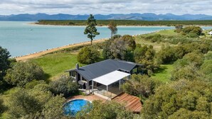 A modern house with a large deck, a swimming pool, and a view of a beach and mountains.