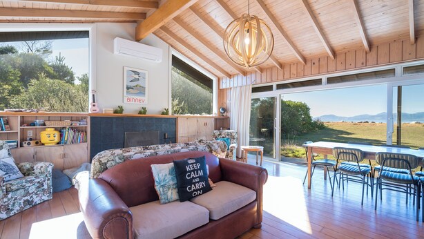 A spacious living area with a wooden ceiling, a sofa with a cushion, a coffee table, and a dining set.