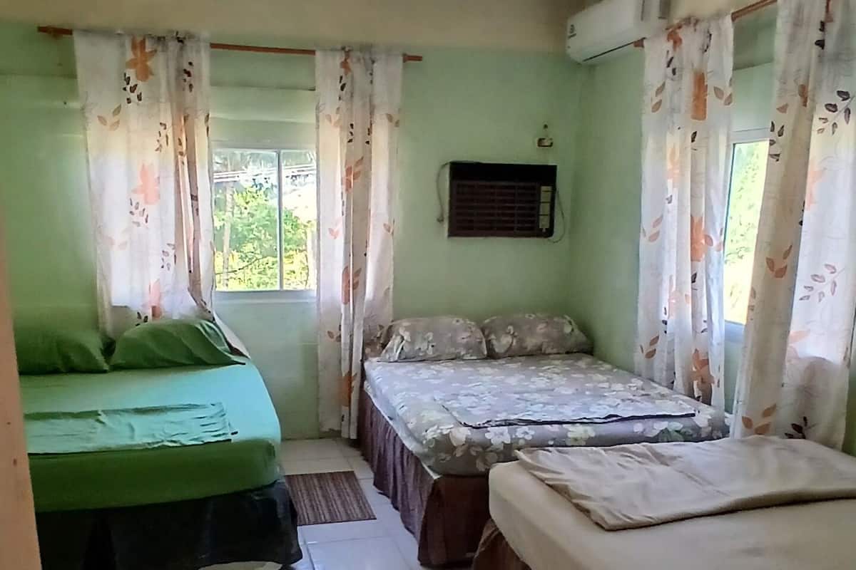 A room with two beds, a window with curtains, a ceiling fan, and a tiled floor.