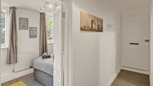 A bedroom with a bed, a window with curtains, a radiator, and a painting on the wall. - Hidden Gem in Battersea (Greater London)