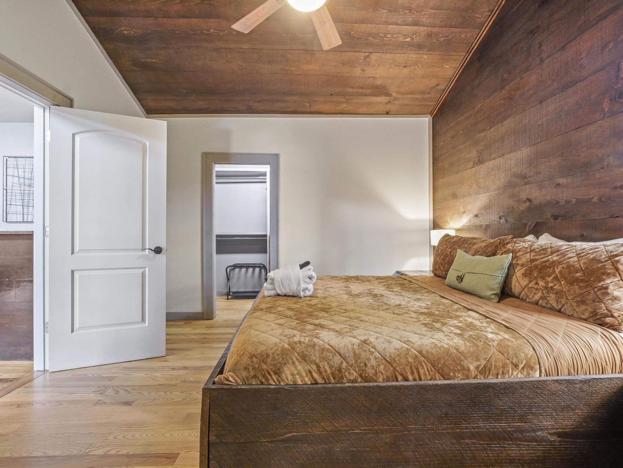 Quarto com teto de madeira, cama com colcha acolchoada, mesa de cabeceira e criado-mudo.