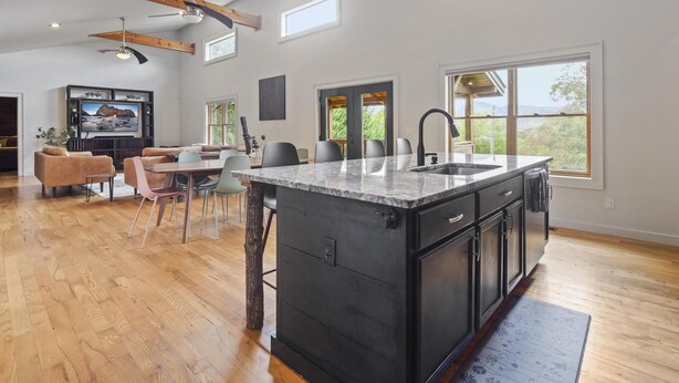 A spacious kitchen with a large island, wooden ceiling beams, and a dining area with a TV and seating.