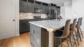A modern kitchen with dark cabinets, a granite countertop, and a central island with bar stools.