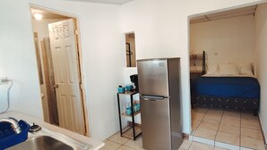 Habitación pequeña con kitchenette, cama y baño.