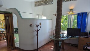 A room with a curved glass partition, a coat rack, a desk with a computer, a television, and a window with blue curtains.