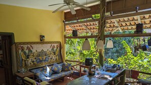 A room with a large mural, a dining area with a bar, and a view of lush greenery.