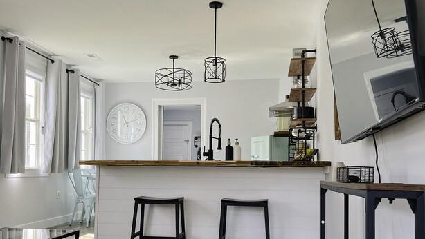 Een moderne keuken met een centraal eiland, twee barkrukken, een plafondventilator, hanglampen en een grote spiegel.