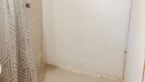 Un área de ducha pequeña y cerrada, con suelo de baldosas y cortina.