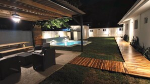 Un patio trasero con terraza de madera, bañera de hidromasaje y zona de barbacoa.