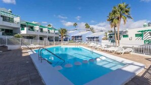 Una piscina con lettini, palme e un edificio con tetto verde.