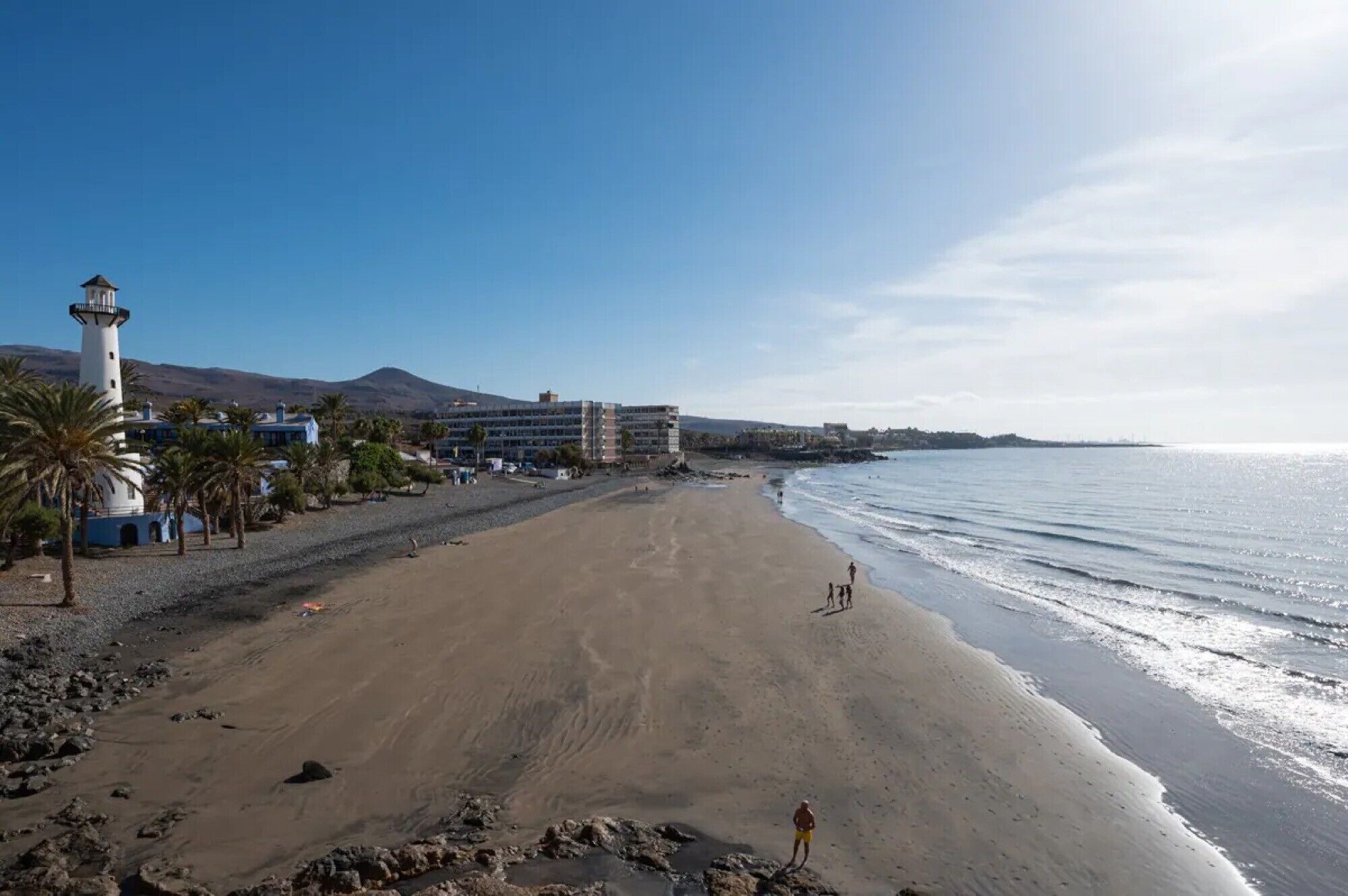 Une plage avec un phare, un bâtiment à étages et un ciel dégagé.