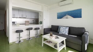Un ambiente compatto con angolo cottura, divano, tavolino e zona con sgabello da bar.