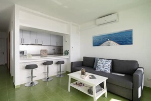 A compact living space with a kitchenette, a sofa, a coffee table, and a bar stool area.