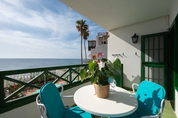 A balcony with a white table and chairs, a potted plant, and a view of the sea.