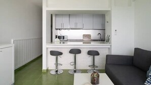Una cucina compatta con forno a microonde, macchina del caffè e un piccolo bancone con sgabelli da bar.