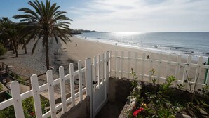 Una spiaggia con una recinzione bianca, palme e cielo sereno.