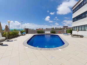 Une piscine sur le toit, dotée de chaises longues et de parasols, entourée d’immeubles et surplombant un ciel dégagé.